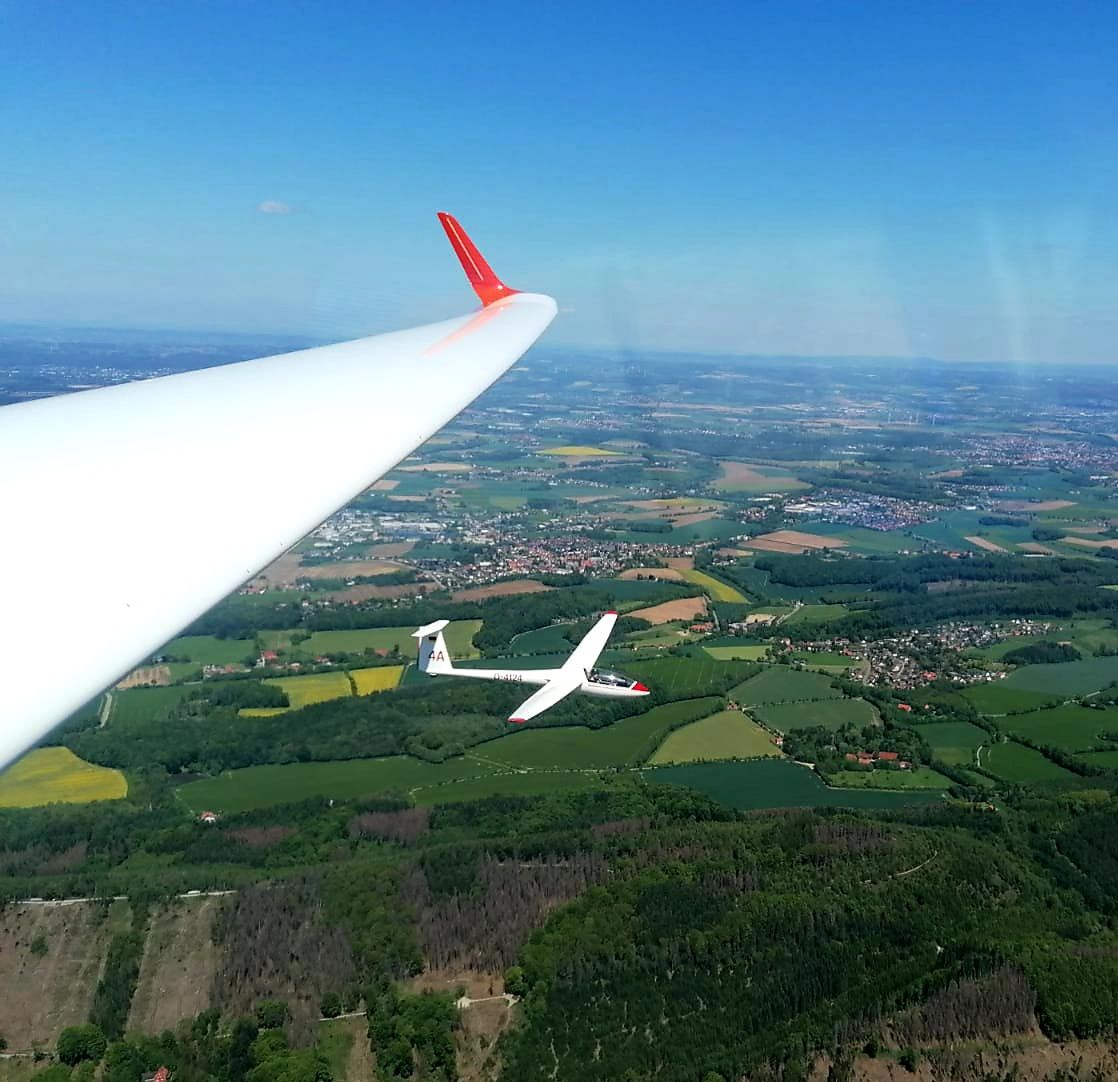 Blick über die Tragfläche eines Segelflugzeugs auf die Landschaft, im Hintergrund ein zweiter Segler